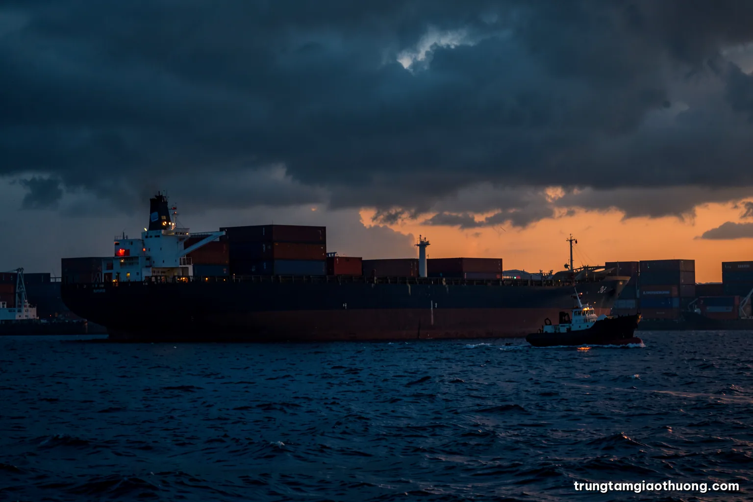 Silhouette of a large container ship at anchor on a stormy sea at dusk, a tugboat approaching, heavy clouds, moody slate blue and deep orange palette